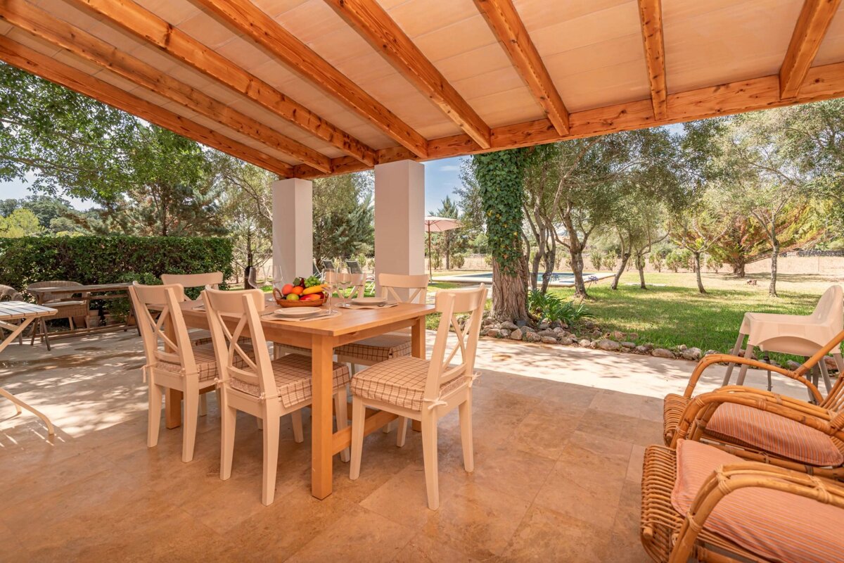 A table with a bowl of fruit on it sits under a wooden roof
