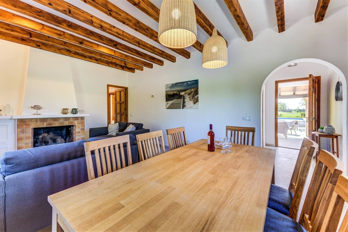Rustic dining room and living area with exposed wooden beams, a fireplace, and an archway leading to an outdoor patio with a pool.