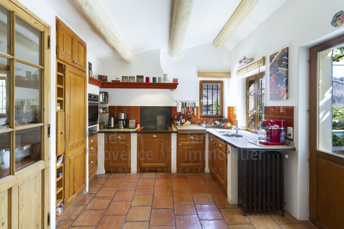 A kitchen with wooden cabinets and red tile floors has the word provence on the wall