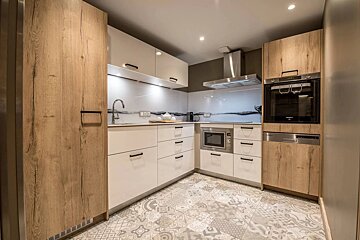 A modern L-shaped kitchen featuring wood and white cabinets, stainless steel appliances, and patterned floor tiles.