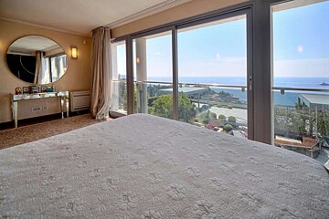 Bright bedroom with a comfy bed, large glass doors revealing a panoramic ocean view, and a mirrored vanity table.