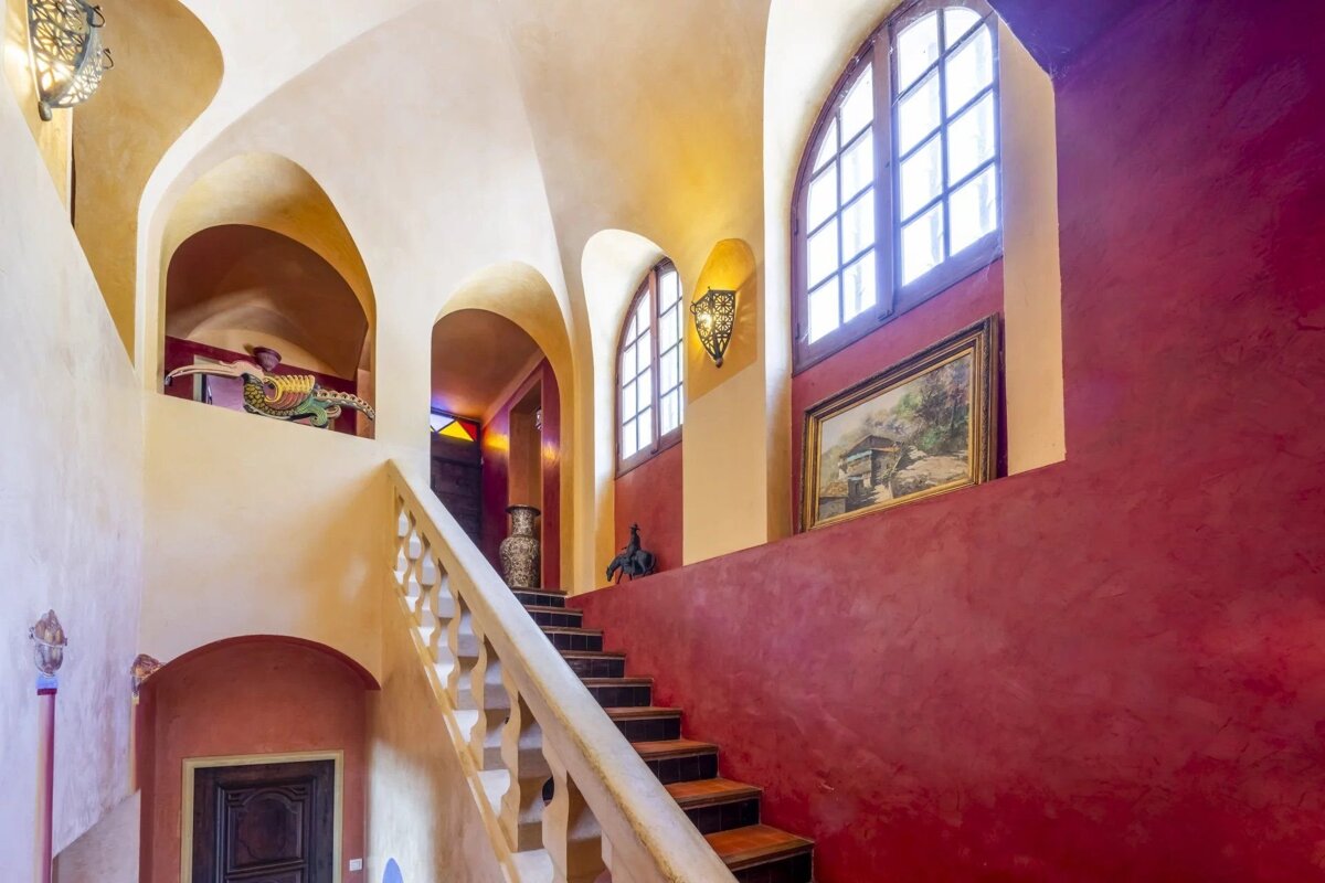 Vibrant Moroccan-style staircase with red and yellow textured walls, vaulted ceilings, arched windows, and decorative accents.