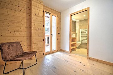 A rustic room with wood paneling, a brown chair, glass double doors, and an open doorway leading into a bathroom.