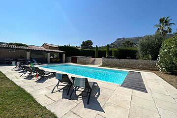 A large swimming pool is surrounded by chairs and a gazebo