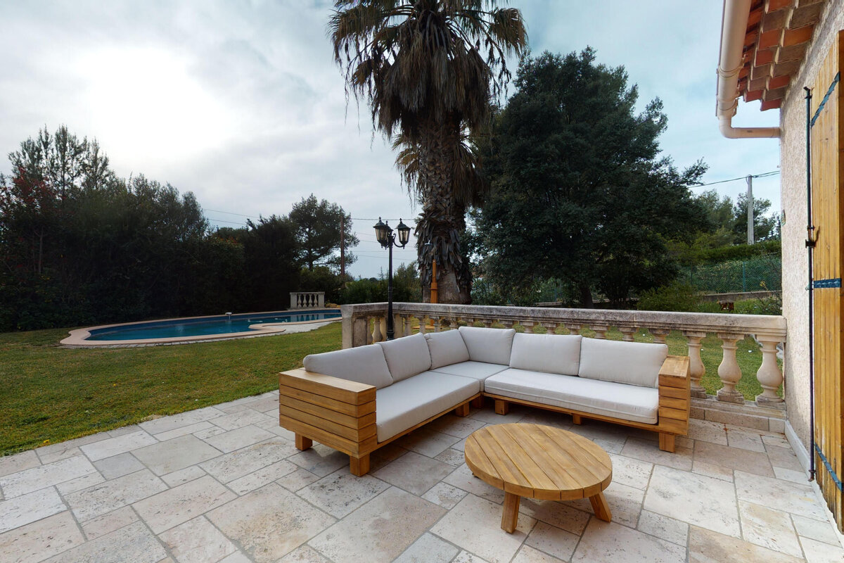 A patio with a couch and a table with a pool in the background