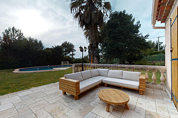 A patio with a couch and a table with a pool in the background