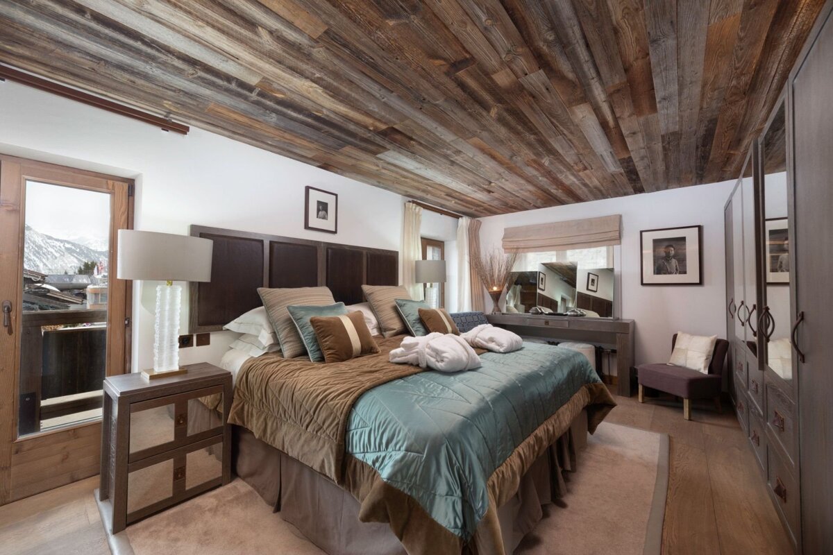 Rustic chic bedroom featuring a wooden ceiling, plush bed, and mountain views from a balcony.
