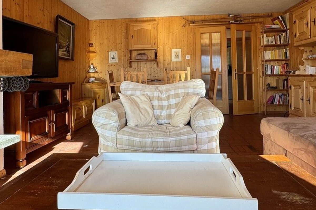 Cozy, wood-paneled cabin living room with a plaid armchair, a white serving tray in the foreground, and rustic wood furniture.