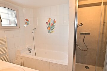A bathroom with a bathtub and a shower with flowers on the wall