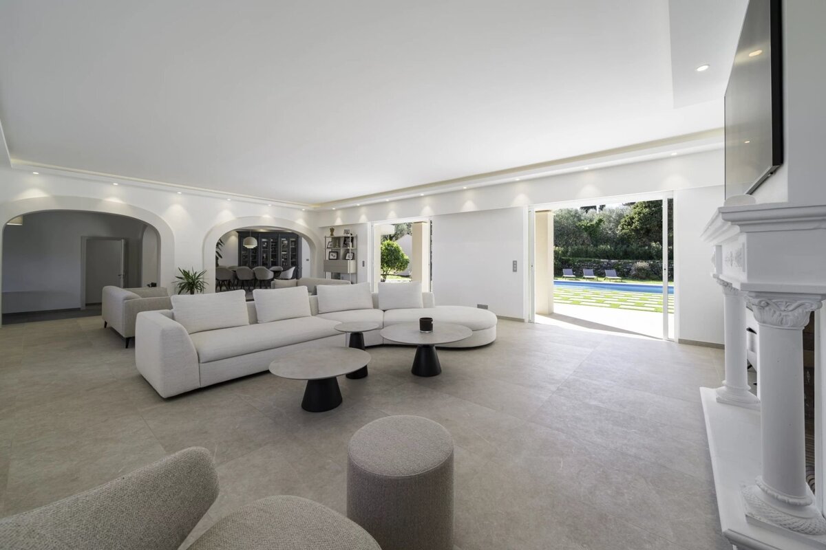Bright, modern living room with a white sectional sofa, coffee tables, and large sliding doors opening to a backyard pool.