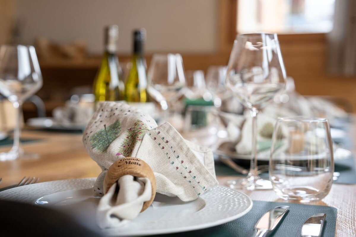 Elegant table setting featuring patterned linen napkins in wooden rings, white plates, and wine glasses on a wooden dining table.