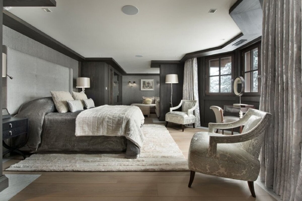 Luxurious modern bedroom in muted grey and neutral tones, featuring a large bed, elegant seating, dark wood accents, and a snowy window view.