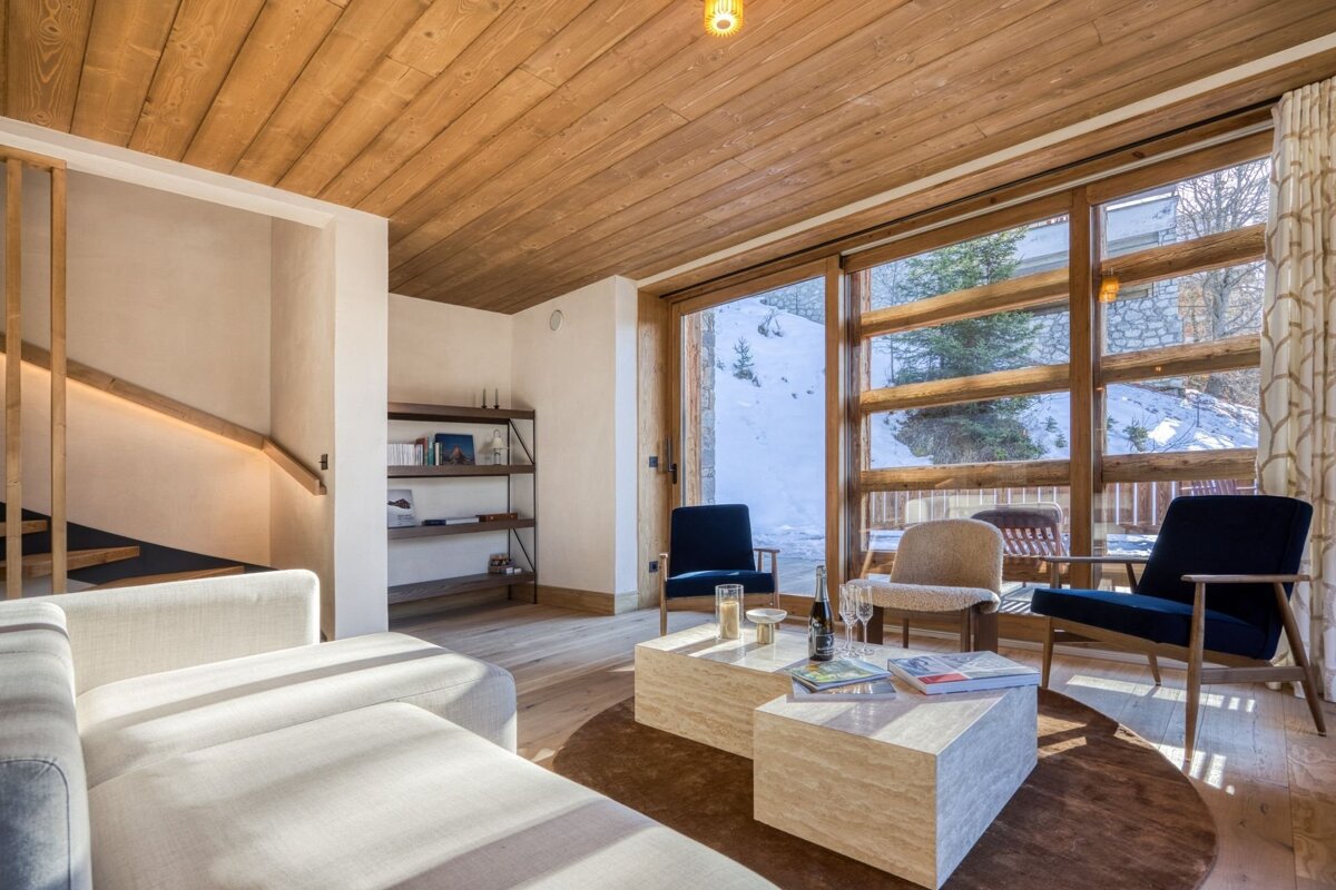 Cozy chalet living room with a warm wood interior, modern furniture, and large windows offering a beautiful snowy mountain view.