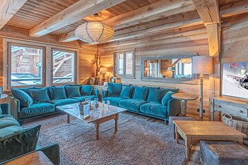 A cozy wooden chalet living room featuring plush teal velvet sofas, rustic wooden furniture, and warm, inviting lighting.