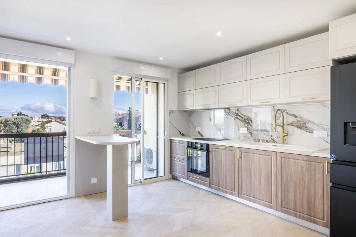 A bright, modern kitchen with white & wood cabinets, marble backsplash, gold faucet, black fridge, and balcony access with city views.