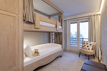 Two teddy bears sit on a bunk bed next to a chair