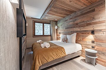 Cozy chalet-style bedroom with rustic wood-paneled walls and ceiling, a bed with white linens, and a mustard yellow throw blanket.