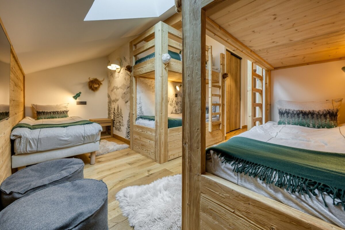 Warm, rustic bedroom with light wood bunk beds, a single bed, mountain wallpaper, and fluffy rugs for a cozy, cabin-like feel.