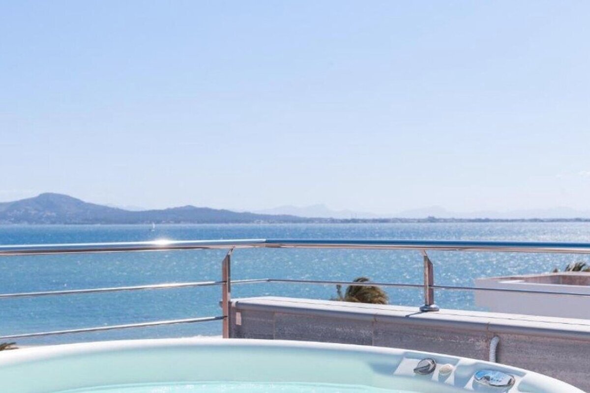 A scenic rooftop hot tub overlooking a sparkling blue ocean with distant mountains under a clear sky.