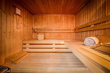 An empty, warm-toned wooden sauna with tiered benches, a rolled-up towel, and a wooden bucket.