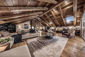 Spacious rustic loft living room with exposed wooden beams, plush seating, a fireplace, and warm lighting.