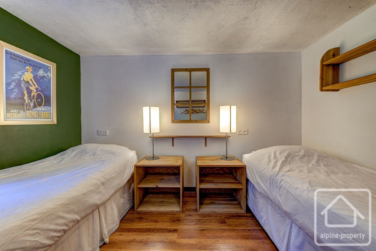 A cozy twin bedroom with two beds, wooden nightstands, lamps, a framed mirror, and a cycling poster on a green accent wall.