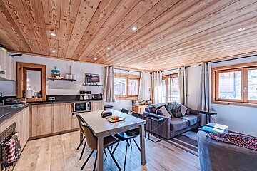 Cozy cabin interior featuring a wood-paneled ceiling, a small kitchen, a dining table, and a living area.