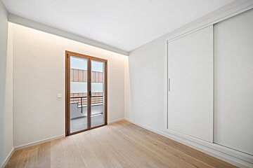 A bright, empty room with light wood flooring, white walls, a wooden balcony door, white sliding closet, and subtle cove lighting along the left wall.