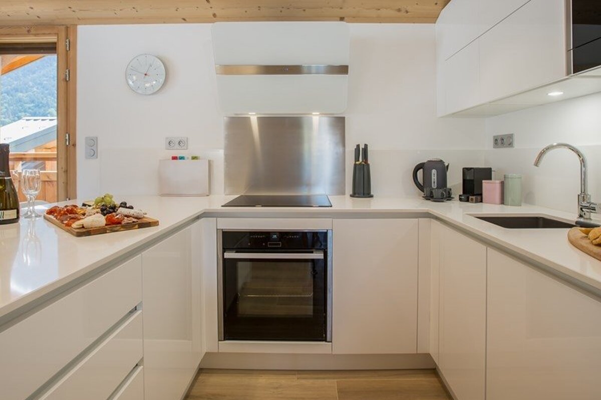 A modern, clean white kitchen with a built-in oven, white countertops, and a charcuterie platter on the left counter.