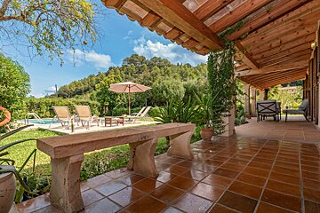 A patio with a bench and chairs and a pool in the background