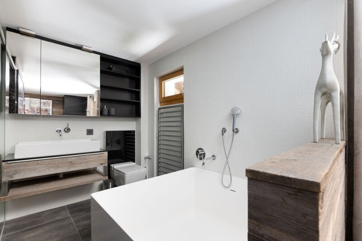 Modern bathroom with a white rectangular bathtub, wooden vanity, large mirror, and a white deer figurine on a rustic wooden partition.