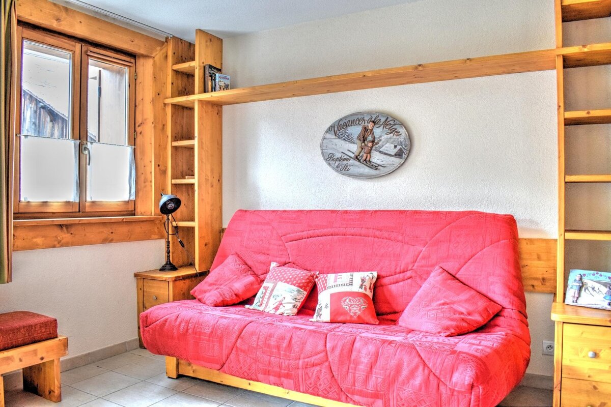 A cozy room with a vibrant red sofa, integrated wooden shelving, and a window. Ski-themed wall art adds to the warm, rustic lodge decor.