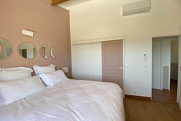 A cozy bedroom featuring a large bed with white bedding, a pink accent wall with decorative moon phase mirrors, a pink sliding door, and wood floors.
