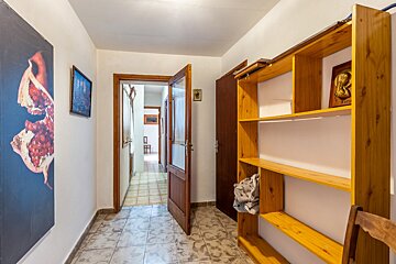 A tiled hallway with white walls, wooden doors, a large pomegranate print on the left, and an empty wooden shelving unit on the right.