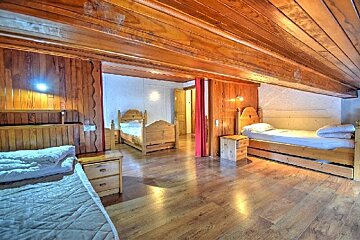 A rustic room with extensive wooden paneling on floors, walls, and ceiling. Features several wooden beds with white bedding and nightstands.