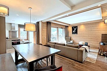 A modern open-plan living/dining/kitchen in a wood-paneled chalet with balcony access, featuring contemporary furnishings and deer art.