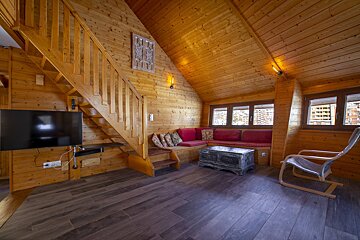 Cozy wooden chalet interior with a rustic living room, staircase, red sectional sofa, and wall-mounted TV.