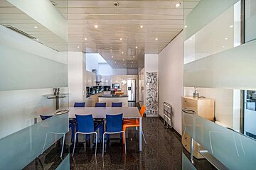 Modern, open-plan dining and kitchen area with glossy black floors, a long table with colorful chairs, and sleek glass partitions.