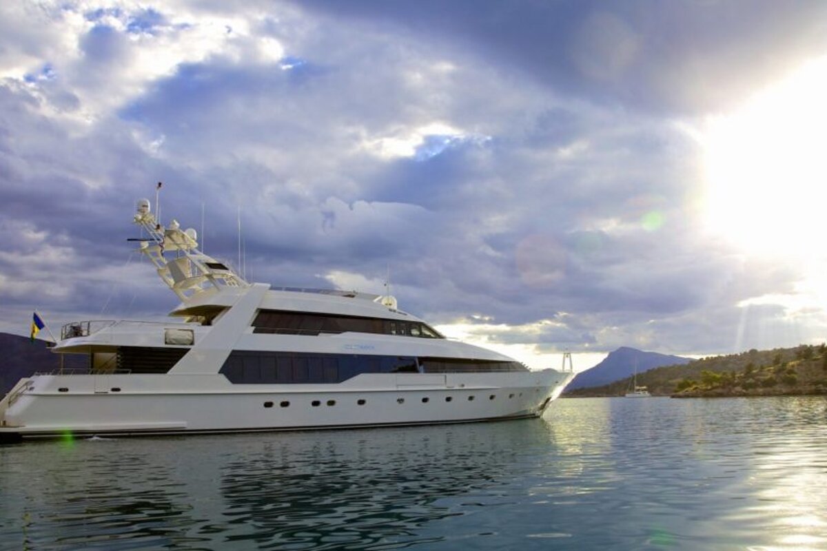 A large white yacht is in the water with mountains in the background