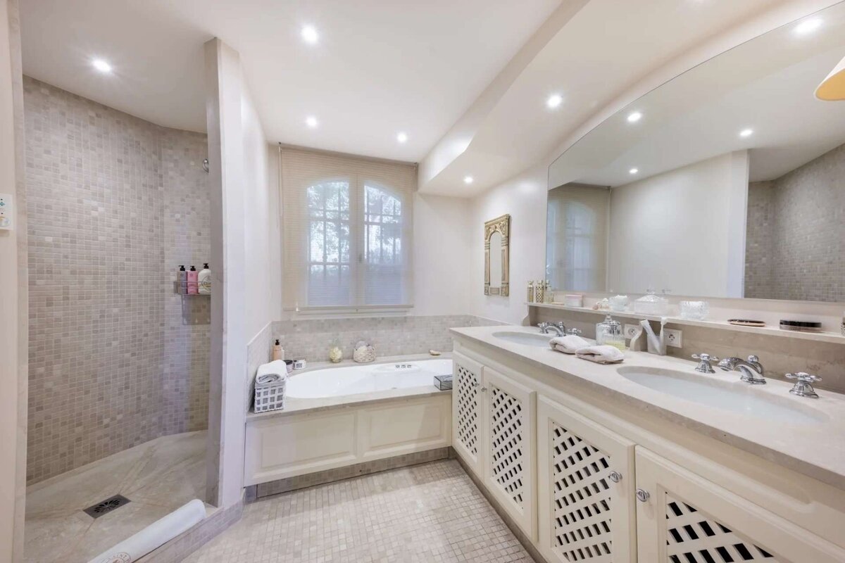A bright, elegant bathroom featuring a tiled walk-in shower, a bathtub by a window, and a double vanity with a large mirror.