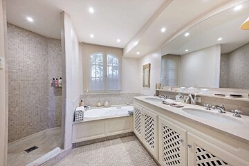 A bright, elegant bathroom featuring a tiled walk-in shower, a bathtub by a window, and a double vanity with a large mirror.