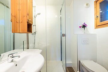 A bright, modern bathroom featuring a white sink, a glass-enclosed shower, a wooden cabinet, and a toilet.