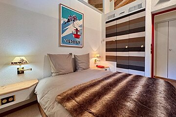 Cozy chalet bedroom featuring a bed with a faux-fur blanket, a vintage Verbier ski poster, and striped closet doors.