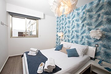A bedroom with a bed and a window with blue leaves on the wall