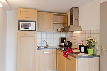 A cozy, modern kitchen featuring light wood cabinets, white tile backsplash, a microwave, sink, stovetop, and appliances on the counter.