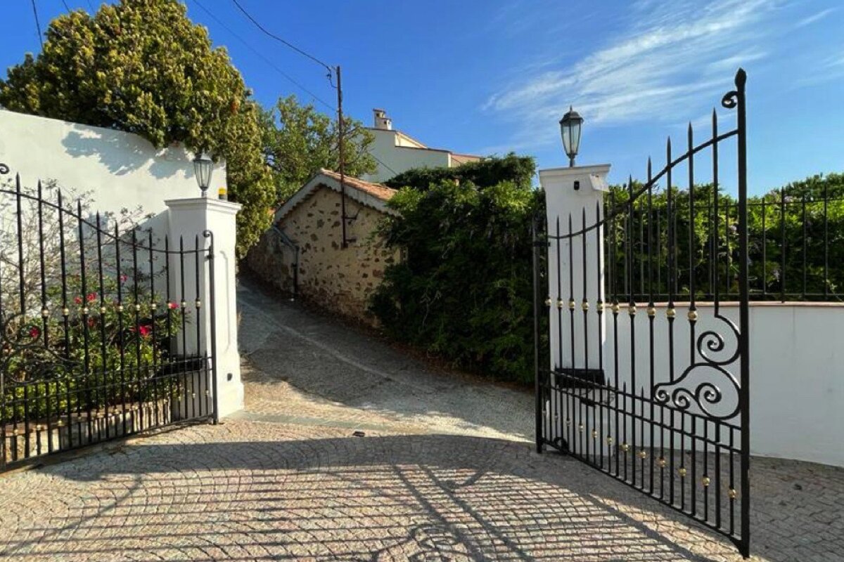 A wrought iron gate is open to a stone driveway