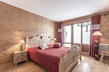 A cozy, wood-paneled bedroom with a red bed, heart-carved furniture, and ski-themed decor, overlooking a snowy landscape.