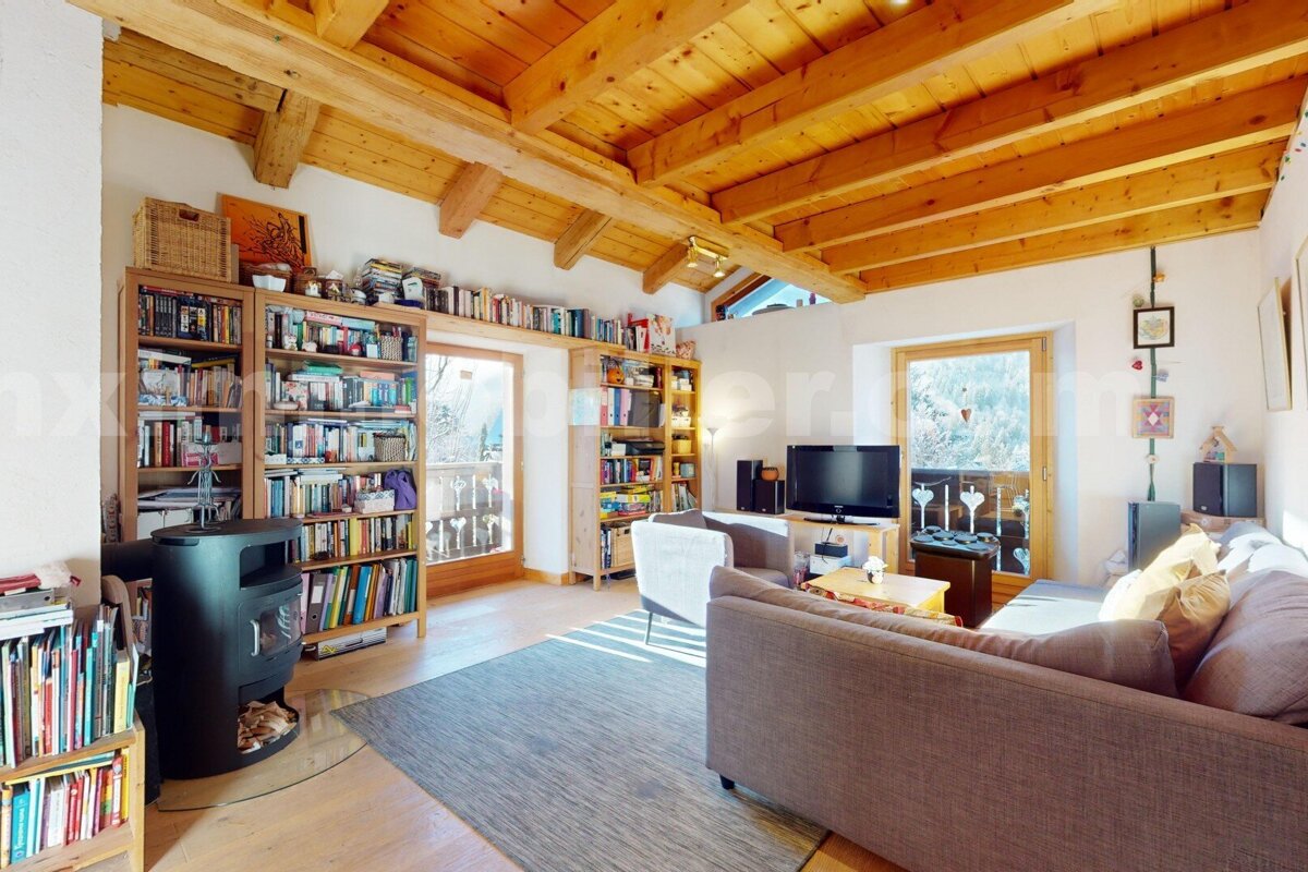 Cozy living room with a wooden beamed ceiling, extensive bookshelves, a wood stove, and comfy seating, opening to balconies with mountain views.