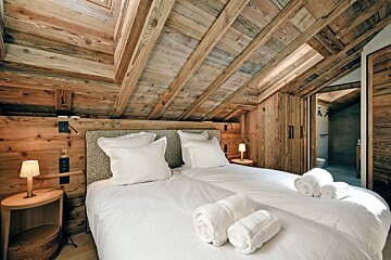 A rustic, cozy attic bedroom with extensive wood paneling on walls and vaulted ceiling. It features two beds with crisp white linen and bedside lamps.