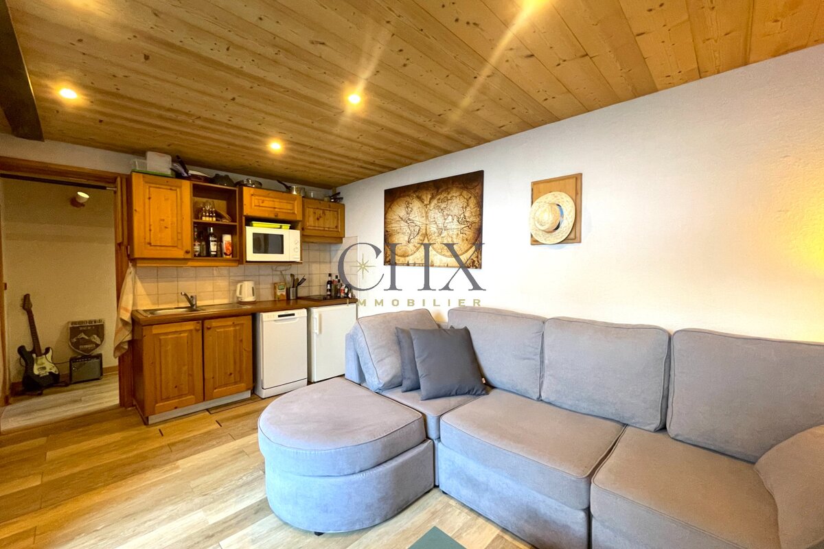 Cozy studio apartment with a wood-plank ceiling, small kitchen, and large grey sectional sofa.